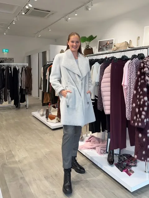 A soft light coat and grey trousers styled in the boutique