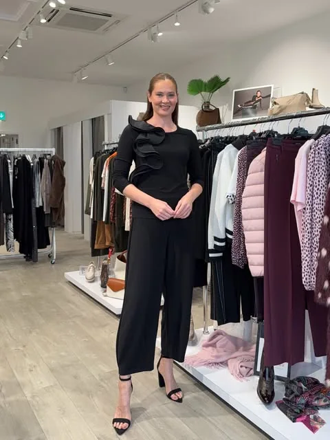 An elegant black jumpsuit with a sculptural ruffled shoulder